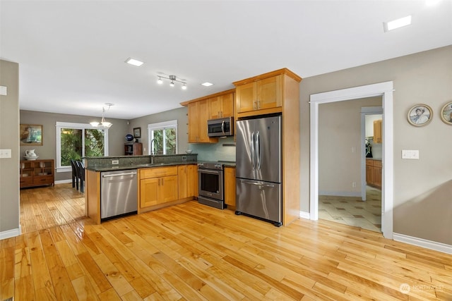 kitchen with stainless steel appliances, light hardwood / wood-style flooring, kitchen peninsula, and pendant lighting