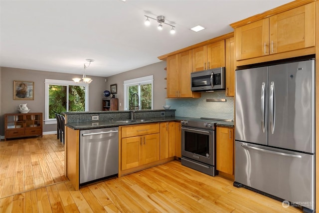 kitchen with light wood-type flooring, stainless steel appliances, dark stone counters, and kitchen peninsula