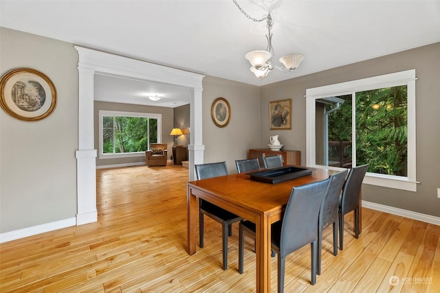 dining area with decorative columns, a chandelier, and light wood-type flooring