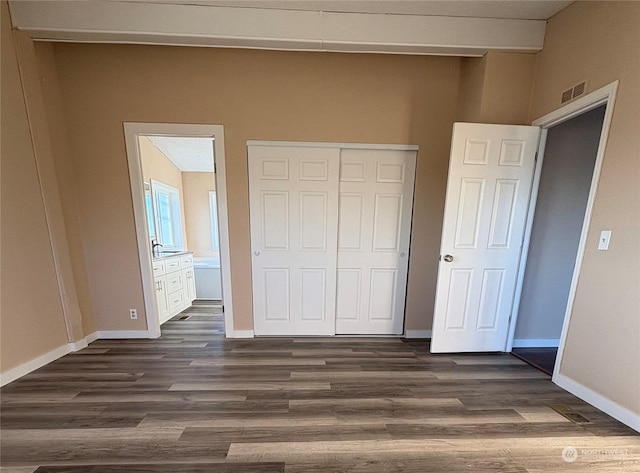 unfurnished bedroom featuring ensuite bathroom, a closet, and dark hardwood / wood-style flooring