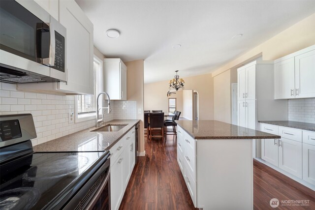 1303 Craig St W, Moses Lake, WA 98837 - kitchen featuring appliances with stainless steel finishes, a chandelier, dark wood finished floors, dark stone countertops, and backsplash