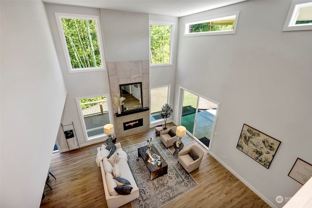 living room with a high ceiling, light hardwood / wood-style flooring, and a tiled fireplace