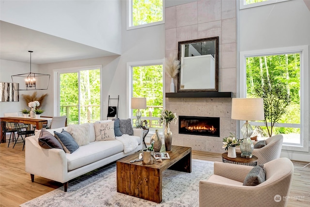 living room featuring a tiled fireplace, plenty of natural light, a towering ceiling, and light hardwood / wood-style flooring