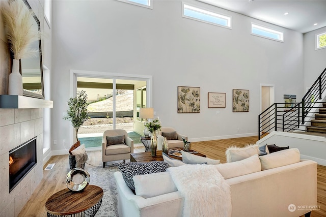 living room featuring light wood-type flooring, a tiled fireplace, and a high ceiling