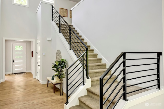 stairs featuring a healthy amount of sunlight, wood-type flooring, and a high ceiling