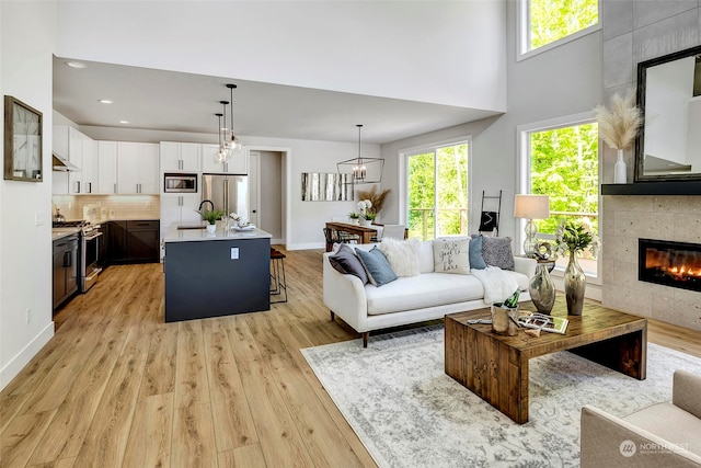 living room featuring a high ceiling, light wood-type flooring, a fireplace, a chandelier, and sink