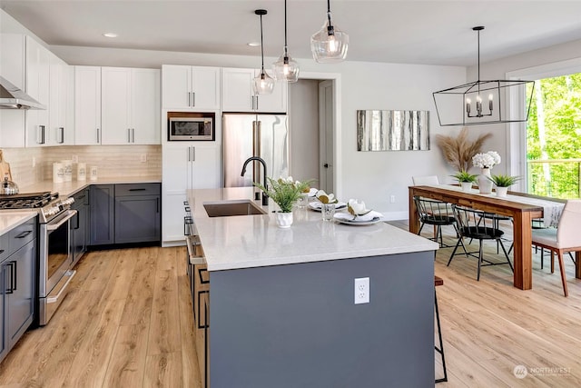 kitchen with decorative light fixtures, appliances with stainless steel finishes, and a kitchen island with sink