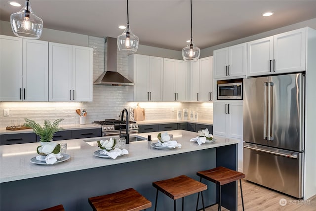 kitchen featuring pendant lighting, white cabinetry, wall chimney range hood, stainless steel appliances, and a kitchen breakfast bar