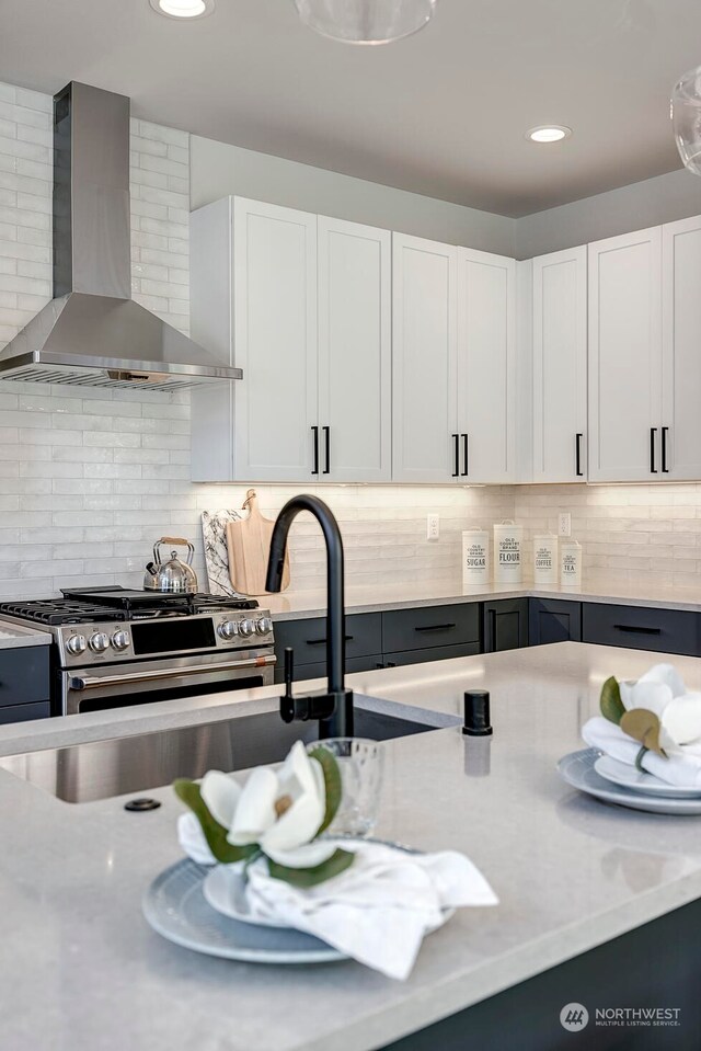 kitchen with decorative backsplash, wall chimney range hood, and white cabinetry