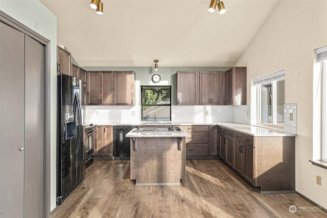 kitchen featuring vaulted ceiling, hardwood / wood-style flooring, a center island, black appliances, and dark brown cabinetry