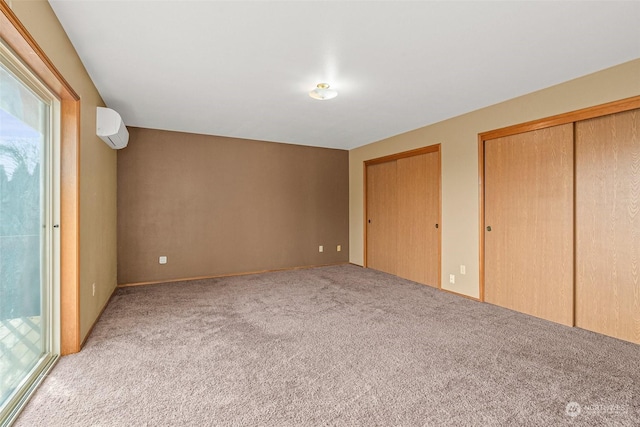 unfurnished bedroom featuring light carpet, multiple closets, an AC wall unit, and access to outside