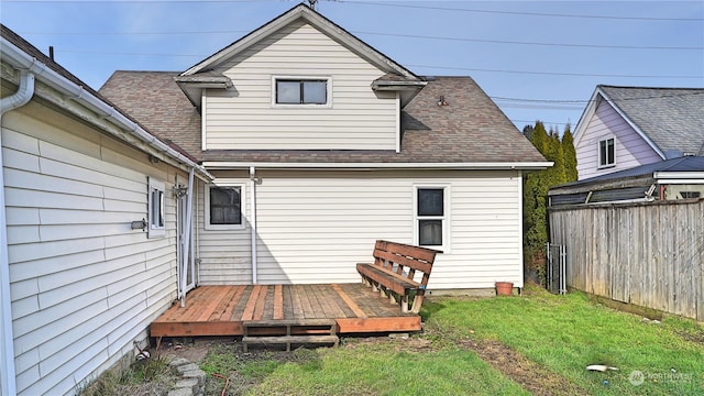 back of property featuring a deck, fence, a lawn, and roof with shingles