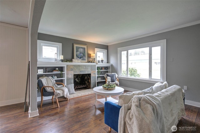 living room featuring a tiled fireplace, baseboards, hardwood / wood-style floors, and ornamental molding