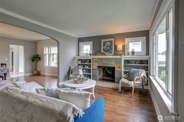 living room with baseboards, ornamental molding, a fireplace, wood finished floors, and arched walkways