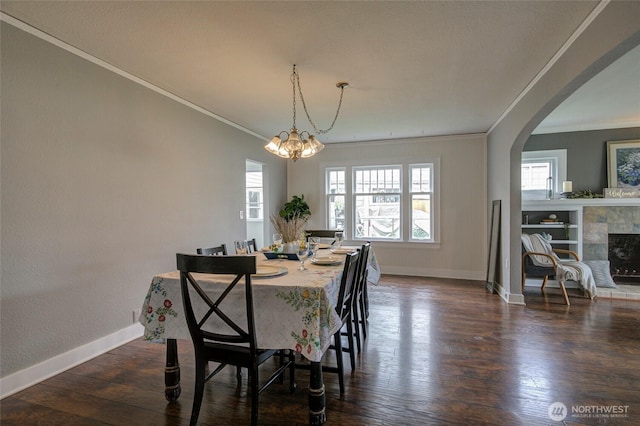 dining room featuring baseboards, arched walkways, dark wood-type flooring, and a fireplace