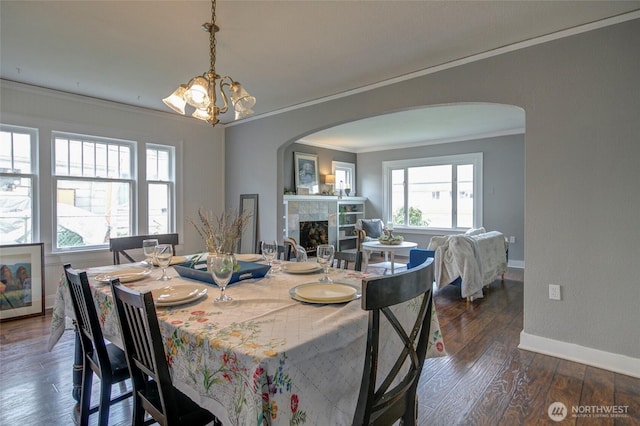 dining area featuring arched walkways, dark wood-style floors, a fireplace, and baseboards