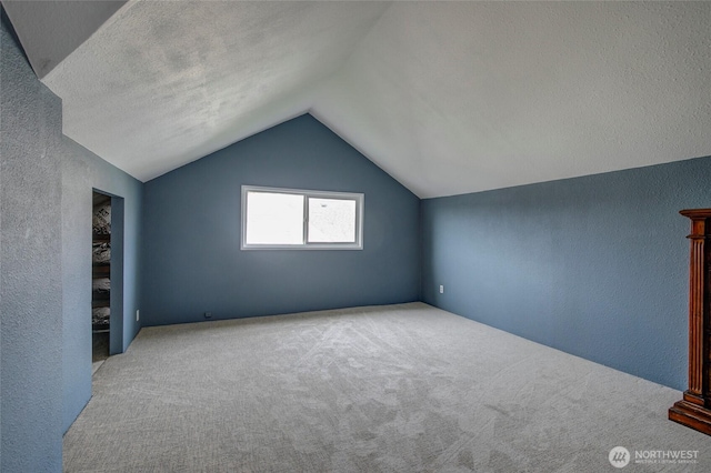 additional living space featuring a textured wall, carpet floors, a textured ceiling, and vaulted ceiling