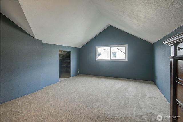 additional living space with a textured wall, a textured ceiling, lofted ceiling, and carpet floors