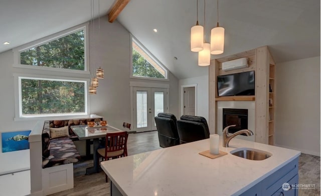 kitchen featuring sink, hanging light fixtures, a kitchen island with sink, beam ceiling, and a wall mounted air conditioner