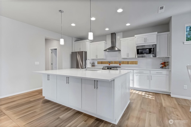 kitchen featuring an island with sink, white cabinets, wall chimney range hood, and stainless steel appliances