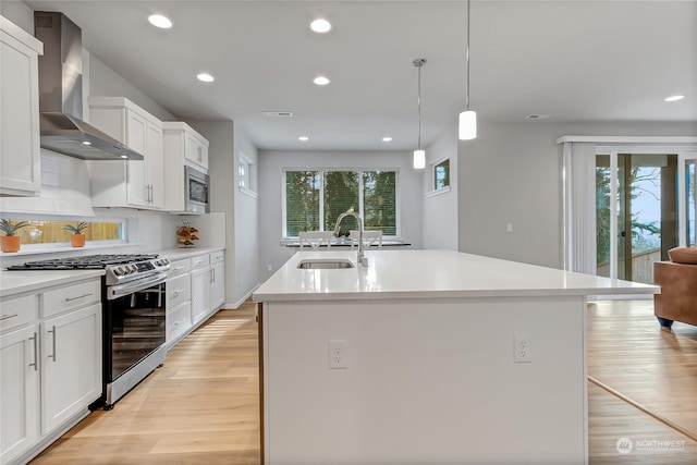 kitchen featuring appliances with stainless steel finishes, hanging light fixtures, wall chimney range hood, sink, and a center island with sink