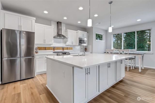 kitchen featuring appliances with stainless steel finishes, wall chimney exhaust hood, sink, white cabinetry, and an island with sink