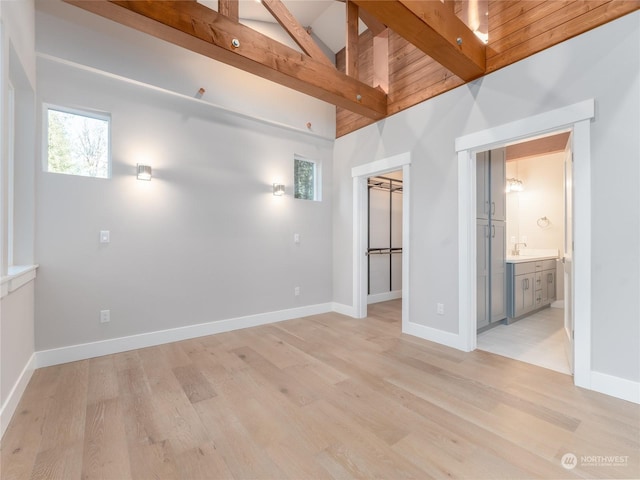 empty room with sink, high vaulted ceiling, beam ceiling, and light hardwood / wood-style floors