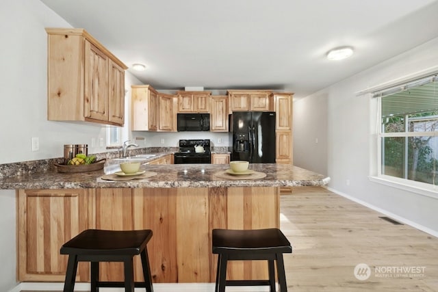 kitchen featuring light brown cabinetry, black appliances, kitchen peninsula, and a breakfast bar