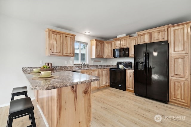 kitchen with a breakfast bar, black appliances, light wood-type flooring, kitchen peninsula, and light brown cabinets