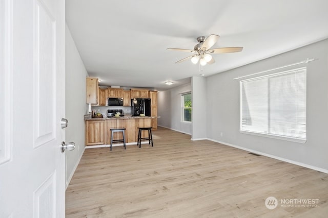 kitchen featuring black appliances, a kitchen bar, ceiling fan, kitchen peninsula, and light hardwood / wood-style flooring