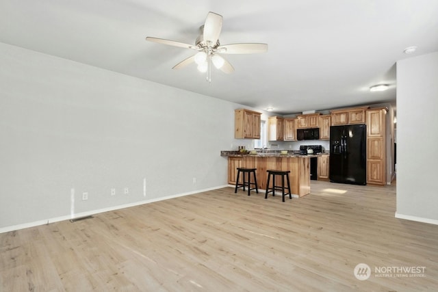 kitchen featuring light wood-type flooring, black appliances, kitchen peninsula, and a kitchen bar