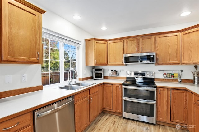 kitchen with appliances with stainless steel finishes, sink, and light wood-type flooring