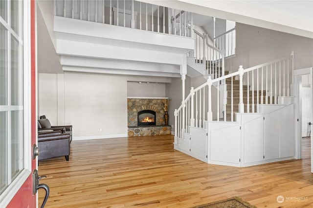 living room featuring a stone fireplace, light hardwood / wood-style floors, and a high ceiling