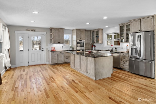 kitchen with stainless steel appliances, a center island, decorative backsplash, dark stone counters, and light wood-type flooring