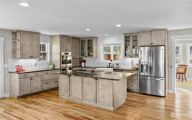 kitchen with light hardwood / wood-style floors, stainless steel appliances, dark stone counters, and a kitchen island