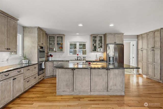 kitchen with stainless steel appliances, a kitchen island, dark stone countertops, and light hardwood / wood-style floors