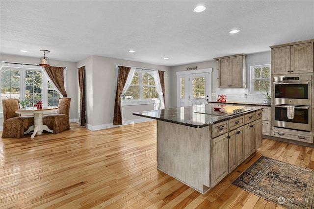 kitchen featuring a kitchen island, a wealth of natural light, double oven, dark stone countertops, and backsplash