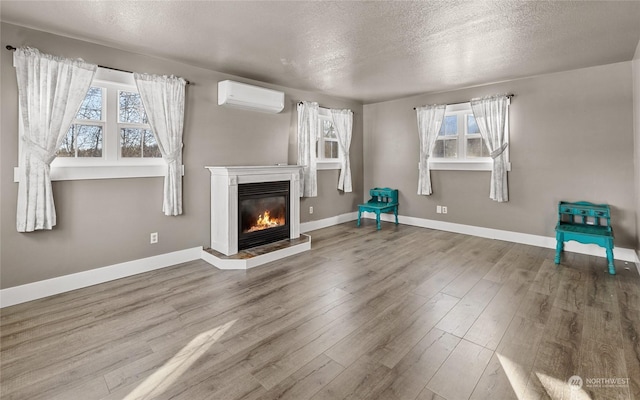 unfurnished living room with a healthy amount of sunlight, a wall mounted air conditioner, hardwood / wood-style floors, and a textured ceiling