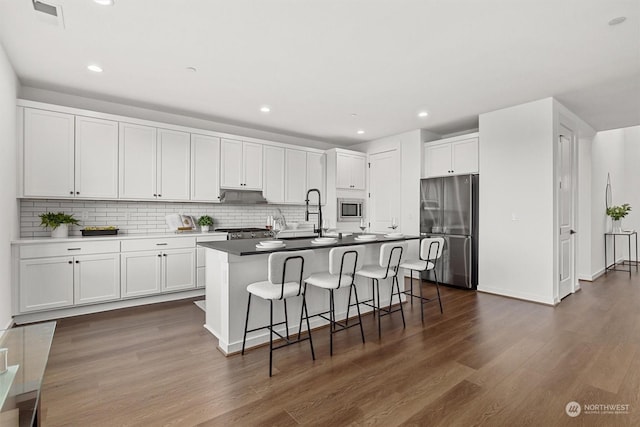 kitchen featuring dark hardwood / wood-style flooring, sink, white cabinets, a center island with sink, and stainless steel appliances