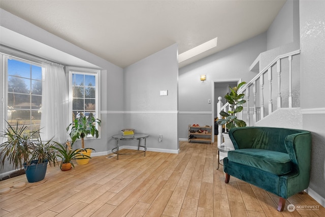 living area featuring vaulted ceiling with skylight and light hardwood / wood-style flooring