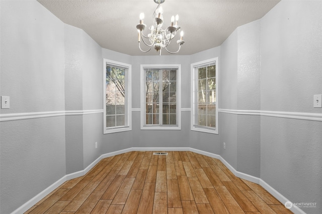 unfurnished dining area featuring a textured ceiling, hardwood / wood-style floors, and a chandelier