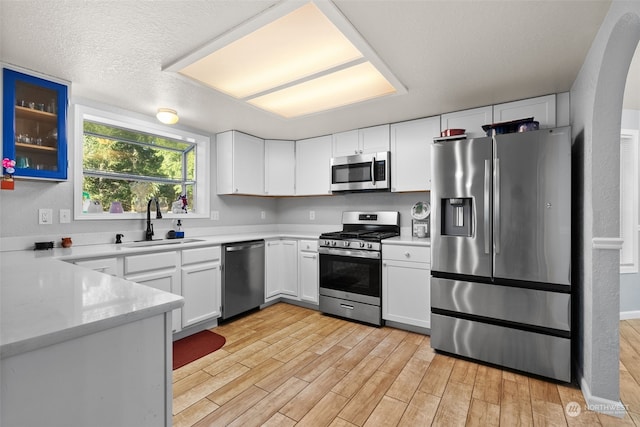 kitchen with a textured ceiling, white cabinetry, stainless steel appliances, sink, and light wood-type flooring