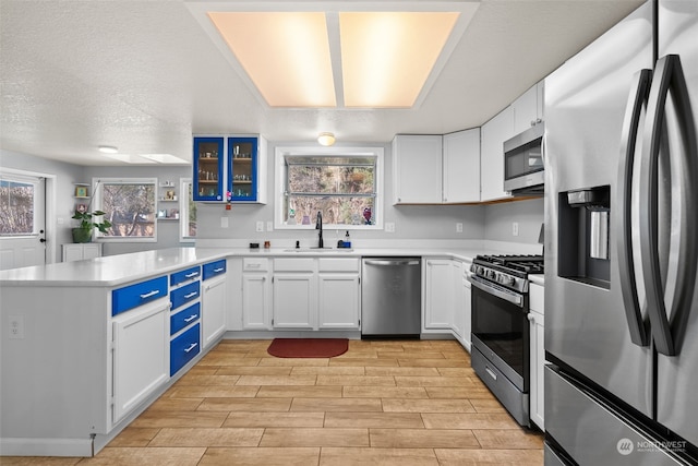 kitchen with blue cabinetry, a textured ceiling, white cabinetry, sink, and stainless steel appliances