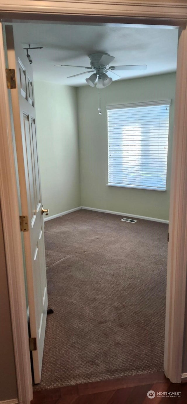 empty room featuring ceiling fan and dark colored carpet