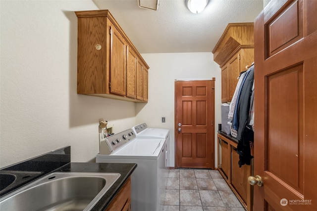 clothes washing area featuring sink, washing machine and clothes dryer, light tile patterned flooring, a textured ceiling, and cabinets