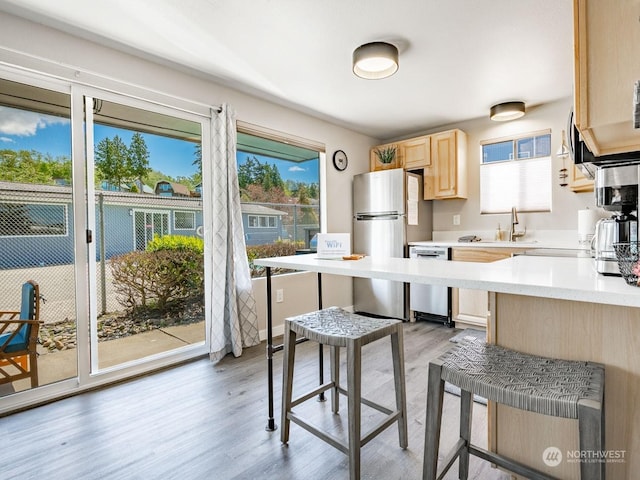 kitchen featuring appliances with stainless steel finishes, light brown cabinets, light wood-type flooring, and kitchen peninsula