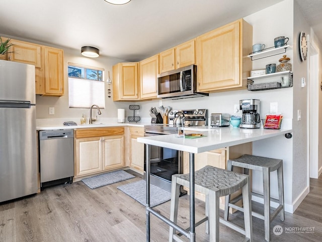 kitchen with sink, light hardwood / wood-style flooring, stainless steel appliances, a kitchen breakfast bar, and light brown cabinets