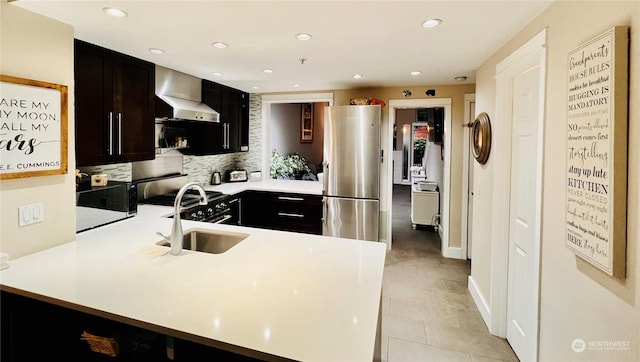 kitchen with kitchen peninsula, sink, tasteful backsplash, wall chimney range hood, and stainless steel appliances