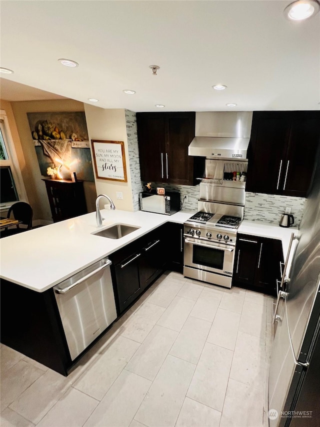 kitchen featuring tasteful backsplash, sink, wall chimney range hood, kitchen peninsula, and stainless steel appliances