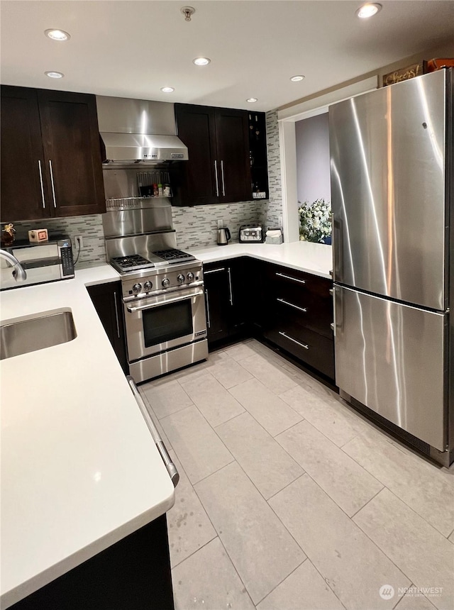 kitchen with wall chimney range hood, stainless steel appliances, sink, backsplash, and light tile patterned floors